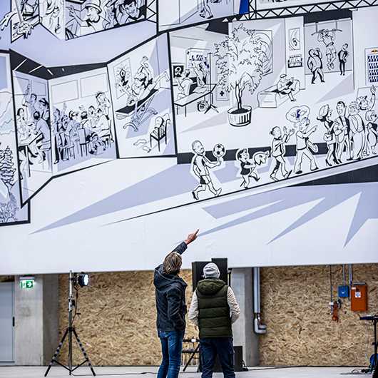 Red Bull Energy Station Oberwang: Großes Wandbild mit Comic-Zeichnungen. Besucher betrachten Kunst.