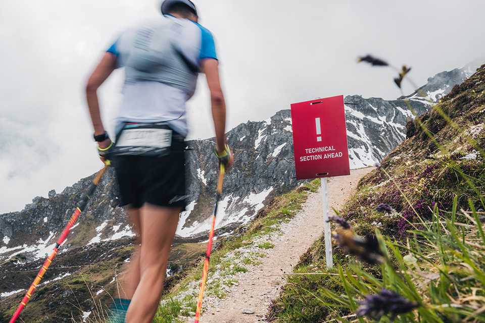 Trail Run WM Innsbruck-Stubai: Läufer auf Bergpfad. Schild Technical Section Ahead.